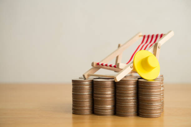 istock Wooden beach chair and hat on heap stack coins with white wall background copy space. 2205966091