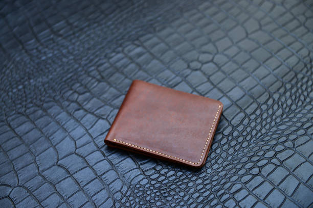 istock A rustic and natural brown pocket size leather wallet, placed on a crocodile texture sheet of black color 2205967035