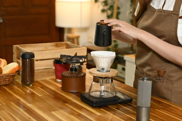 istock A woman is making coffee and pouring it into a cup. The scene is set in a kitchen with various items such as a scale, a cup, a bottle, and a bowl. The woman is wearing an apron. 2205977799