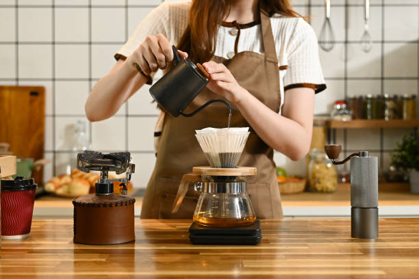 istock A woman is making coffee and pouring it into a cup. The scene is set in a kitchen with various items such as a scale, a cup, a bottle, and a bowl. The woman is wearing an apron. 2205977811
