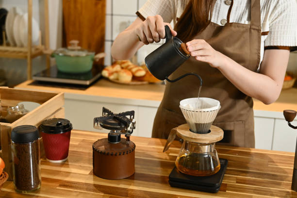 istock A woman is making coffee and pouring it into a cup. The scene is set in a kitchen with various items such as a scale, a cup, a bottle, and a bowl. The woman is wearing an apron. 2205977814