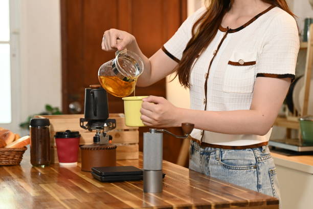istock A woman is making tea in a kitchen. She is wearing an apron and holding a tea strainer. 2205977821