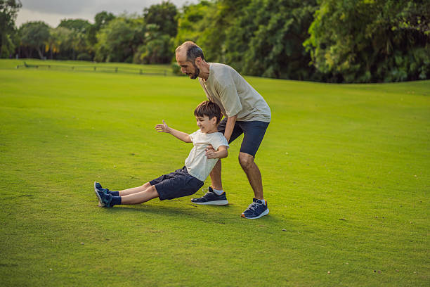 The boy is sitting on the football stand. His father helps him put on his sneakers. Evening light.