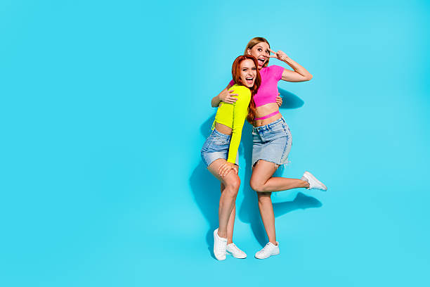 istock Two cheerful young girlfriends posing in bright outfits against a turquoise background, embodying summer fashion and youthful energy 2205990264