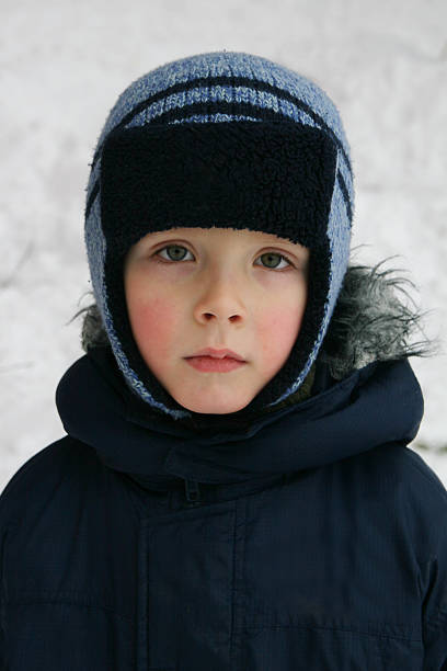 Close-up portrait of a five-year-old boy in winter clothes against a background of snow. A boy in a winter blue hat and jacket.