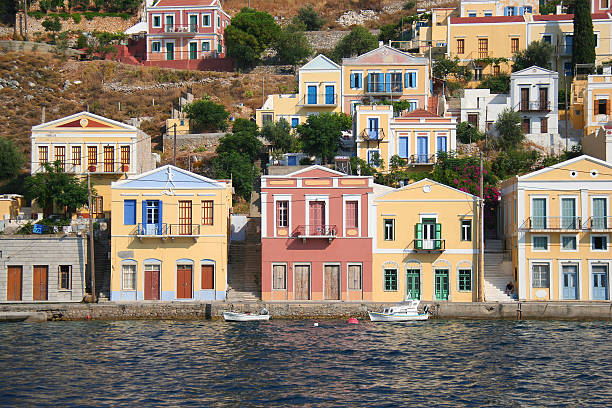 Symi, Greece-July 14,2013:Unidentified Man sitting on steps between Colorful Symi Buildings by the Sea and Wooden Boats