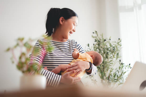 istock Asian woman carrying her baby while working at home office. 2205996355