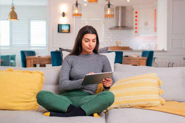 istock Young Woman In Modern Living Room Using Digital Tablet On Comfortable Sofa 2205996910