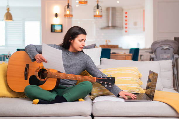 Woman Practicing Guitar and Using Laptop While Working at Home in a Cozy Living Room