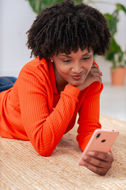 istock Happy African American woman using smartphone while lying on the floor at home. 2205996973