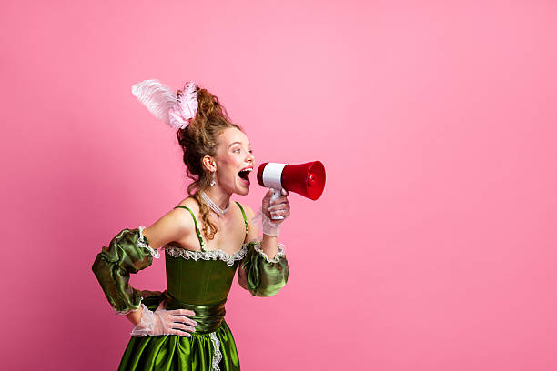 istock Elegant woman in a green baroque gown using a megaphone against a pink backdrop emphasizing modern and historical contrast 2205999779