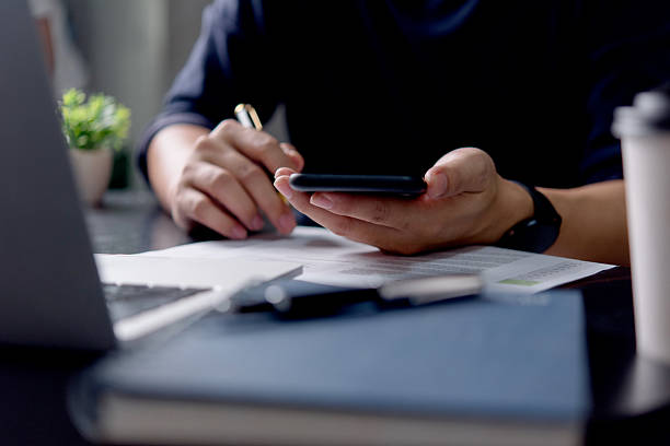 istock A man is using a cell phone while sitting at a desk. Concept of productivity and focus, as the man is engaged in a task on his phone. The laptop on the desk suggests that he may be working 2206002200