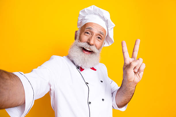 istock Smiling senior male chef posing joyously in uniform before yellow background 2206003333