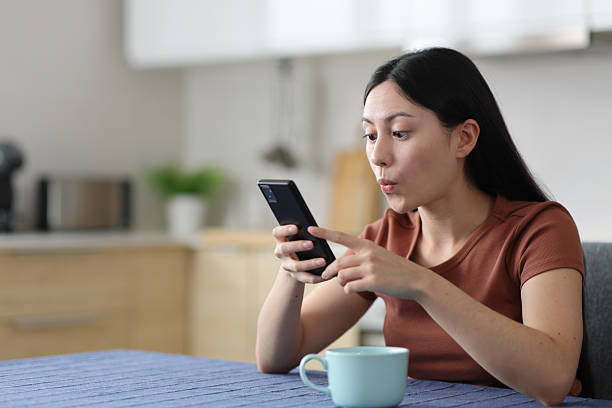 istock Surprised asian woman using smart phone in a kitchen 2206003597