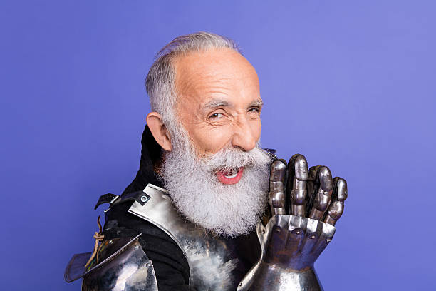 A senior male dressed in medieval inspired armor showing a playful expression while posing gracefully before a vivid purple backdrop, embodying historical charm and whimsical creativity.