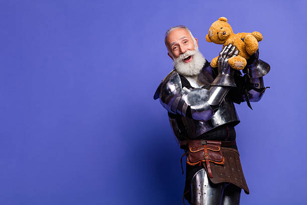 istock Mature knight in full armor holding a teddy bear on a violet backdrop showcasing a humorous and whimsical contrast 2206003836