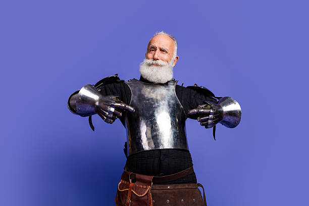 istock Elderly man dressed in medieval knight armor posing against a vibrant purple background 2206003845