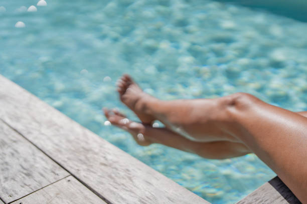 A Hispanic tourist enjoys a carefree summer day by a shimmering pool, leisurely dipping their feet in the water for relaxation and joy during a solo vacation. Embracing individuality and tranquility.