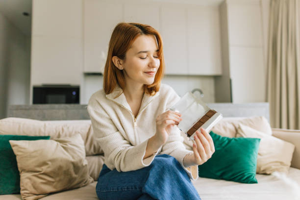 istock Young Woman Enjoying a Chocolate Bar on Sofa at Home 2206006012