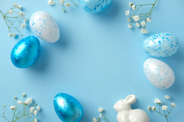 istock Easter frame. Blue speckled eggs, a ceramic bunny, and delicate white flowers on a pastel blue background. 2206009196
