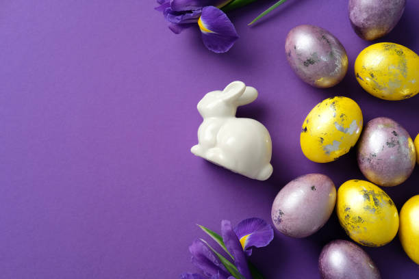 istock Elegant Easter flat lay composition. Ceramic bunny, purple and yellow eggs, and fresh irises on a purple background 2206010377