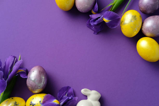 istock Flat lay Easter composition with painted yellow and purple eggs, ceramic bunny, and vibrant irises on a purple background 2206010556