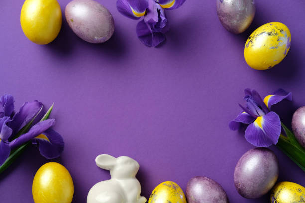 istock Happy Easter greeting card design. Flat lay composition with ceramic bunny, purple and golden Easter eggs, and fresh irises on a purple background. Flat lay, top view 2206010717