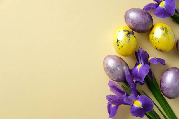 istock Happy Easter greeting card design. Flat lay composition with colorful Easter eggs and blooming purple irises arranged on a pastel yellow background 2206010725