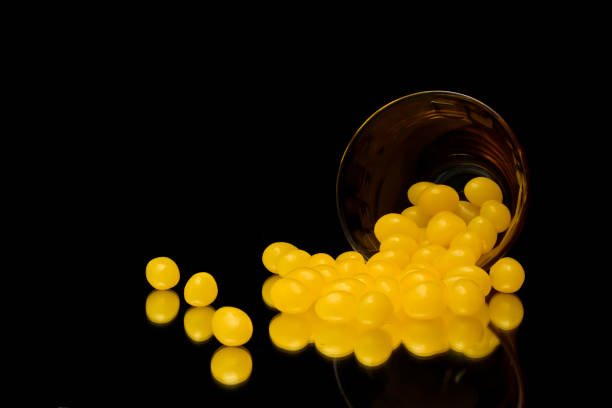 A small glass cup on its side spilling yellow jellybeans onto a mirror