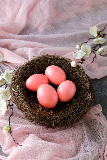 istock Nest with four pink Easter eggs, soft pink fabric background adorned with white flowers. 2206012425