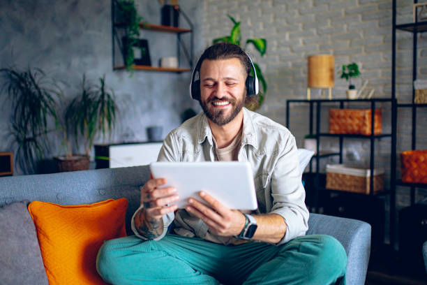 istock Man with headphones using tablet while relaxing in the couch at home 2206012655