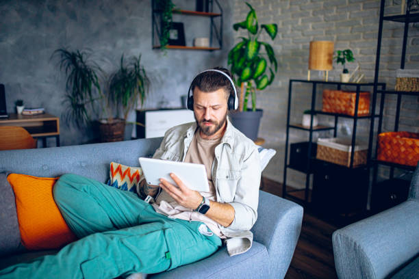 istock Man with headphones using tablet while relaxing in the couch at home 2206013268