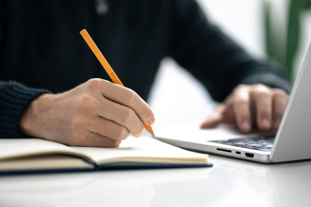 istock Closeup image of a male writing notes in his notebook while using laptop. Boy working on new project 2206013468