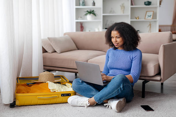 istock Young African American woman using laptop at home while packing for trip 2206013487