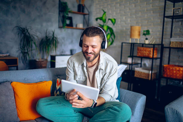 istock Man with headphones using tablet while relaxing in the couch at home 2206013561