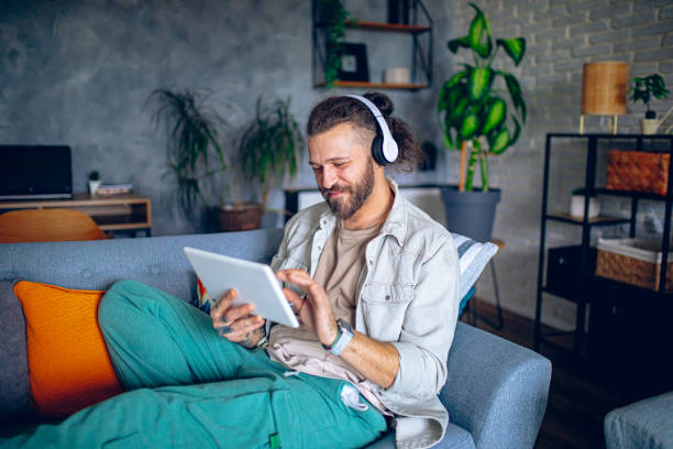istock Man with headphones using tablet while relaxing in the couch at home 2206013834