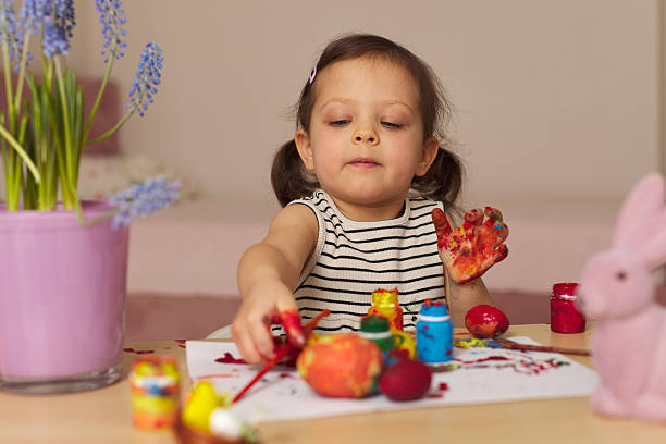 Little child girl paint Easter eggs at home. kid is preparing for Easter.