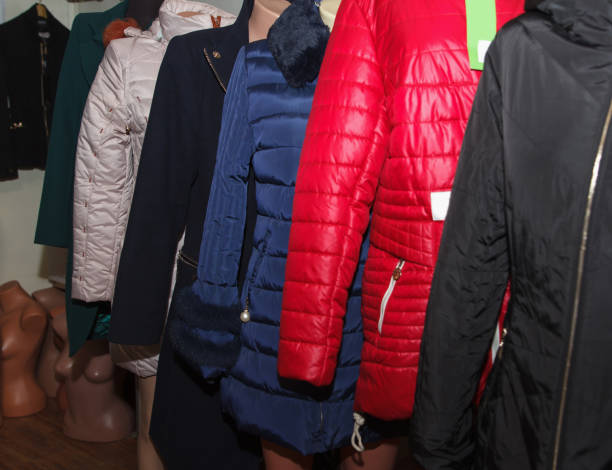 A variety of winter coats, including red, blue, and black, displayed on mannequins in a shop interior, showcasing fashion styles