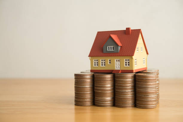 istock House on heap stack coins on wooden table white wall background copy space. 2206021819