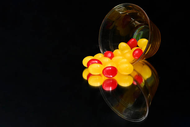 A mixture of red and yellow jellybeans pouring out of a small glass cup