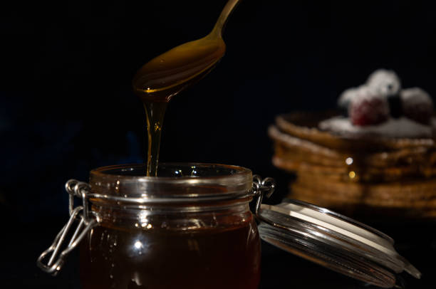 Golden spoon scooping honey from a glass container on a dark background, sweet and viscous fluid with a sweet taste