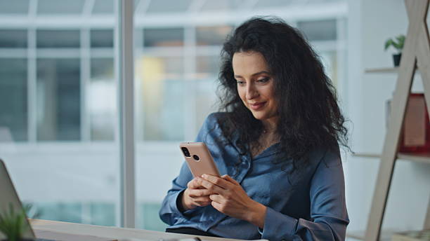 istock Relaxed employee using smartphone at desk. Smiling businesswoman messaging web 2206026070