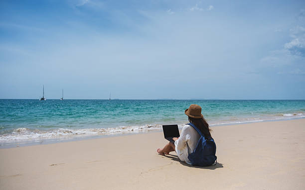 istock A female traveler using and working on laptop computer while sitting on the beach 2206030586
