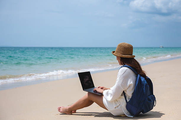 istock A female traveler using and working on laptop computer while sitting on the beach 2206030591