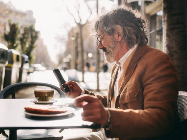 Man Enjoying Coffee and Croissant While Using Smartphone Outdoors in Urban Setting