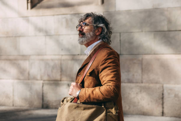 Sophisticated Man in Stylish Apparel Walks Outdoors Carrying a Large Canvas Bag