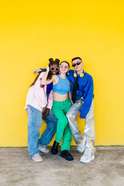 istock Three stylish young adults posing against a vibrant yellow wall, showcasing their unique fashion and personalities 2206037412