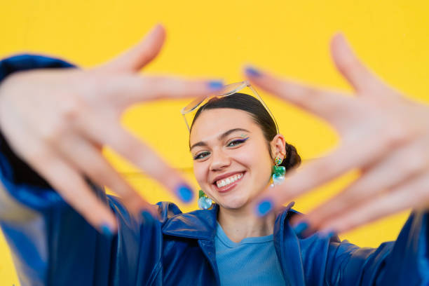Cheerful young woman smiling, framing face with hands against bright yellow backdrop