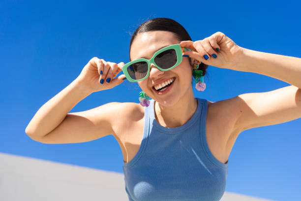 Cheerful woman in sunglasses beaming brightly under cloudless azure sky