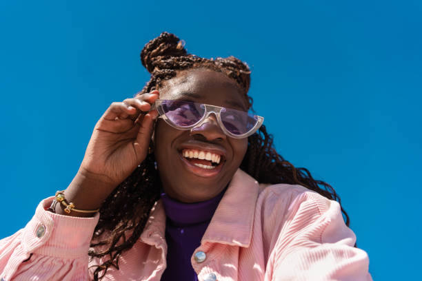 istock Cheerful woman lowering sunglasses, beaming with joy against bright blue sky backdrop 2206037738